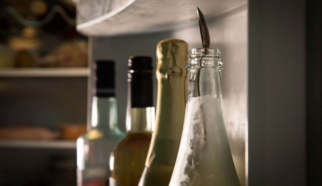 Sektflasche mit einem Silberlöffel steht im Kühlschrank