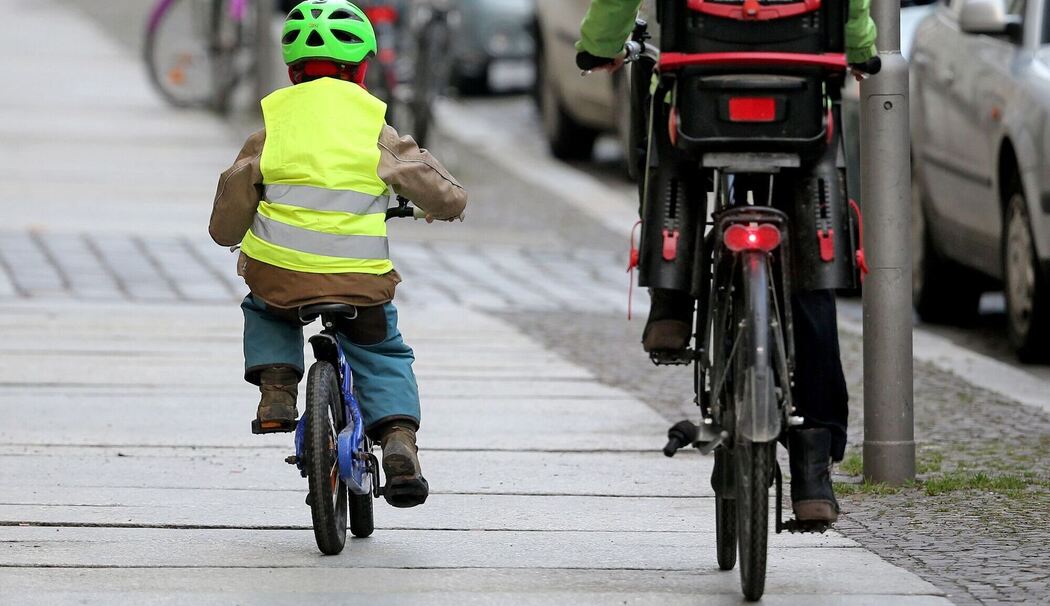 Ein Kind fährt mit dem Rad auf dem Fußweg neben einem Elternteil