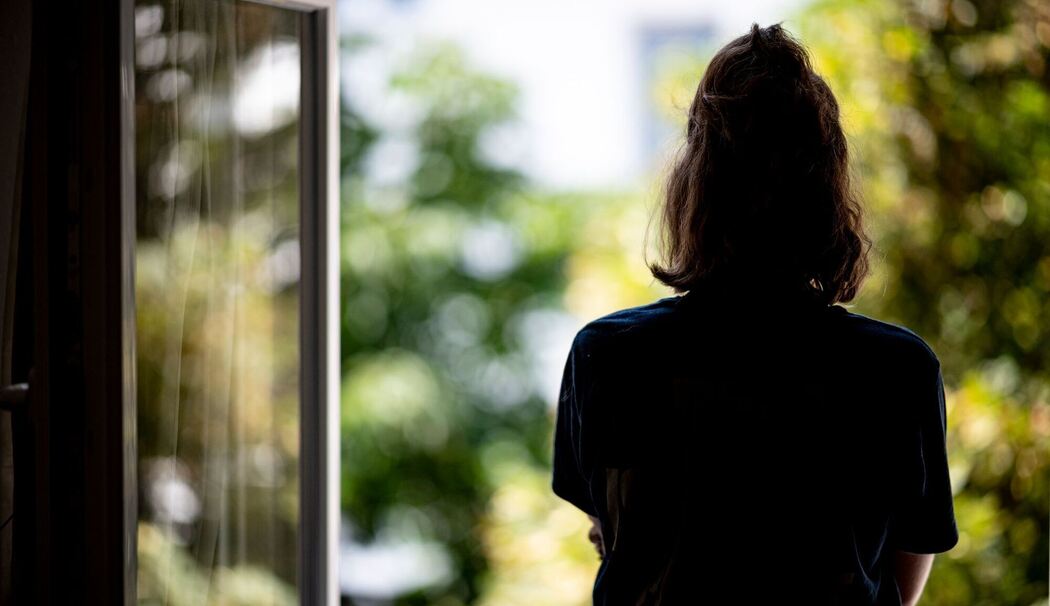 Eine junge Frau steht in ihrer Wohnung an einem Fenster