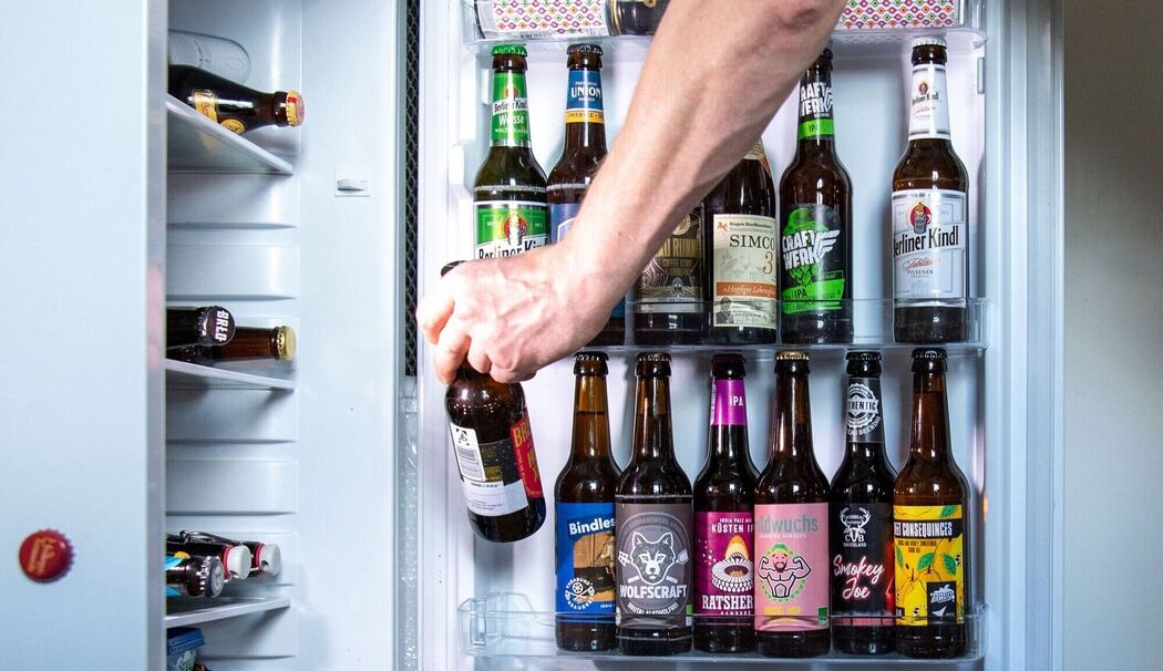 Ein Mann entnimmt ein Bier aus einem Kühlschrank