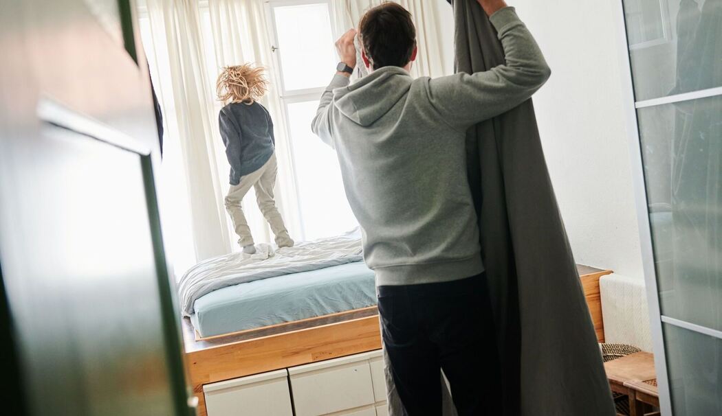 Mann bezieht ein Bett während ein Kind auf dem Bett hüpft