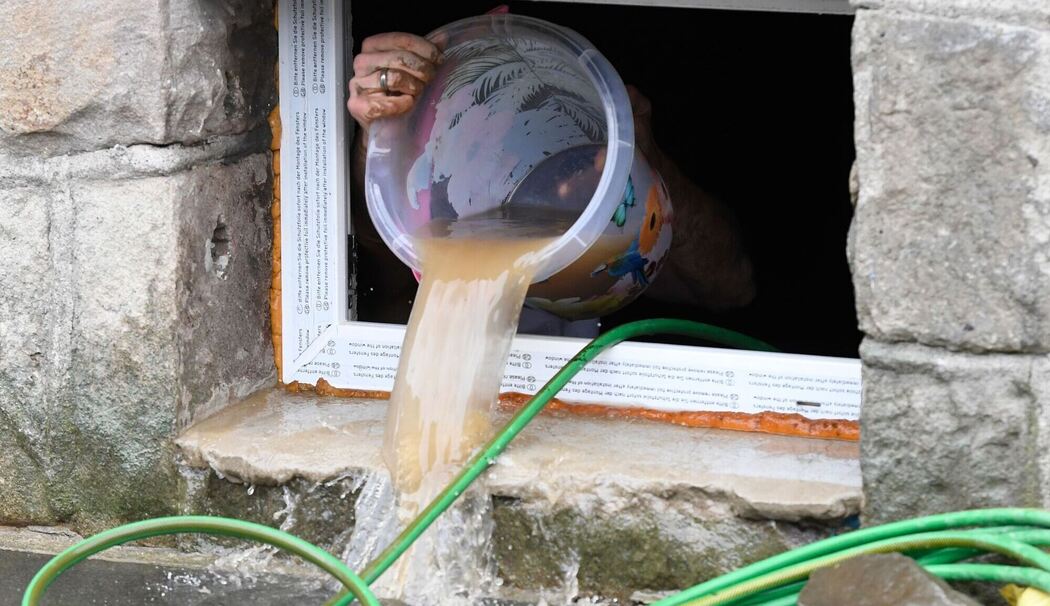 Wasser wird nach Überflutung aus einem Kellerfenster geschüttet