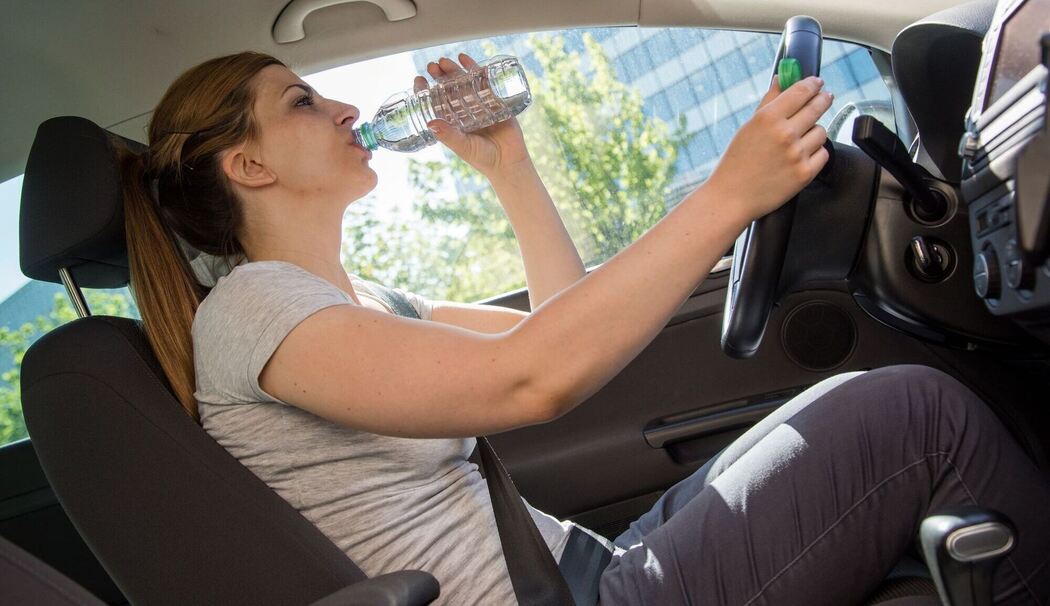 Frau trinkt während der Autofahrt aus einer Wasserflasche