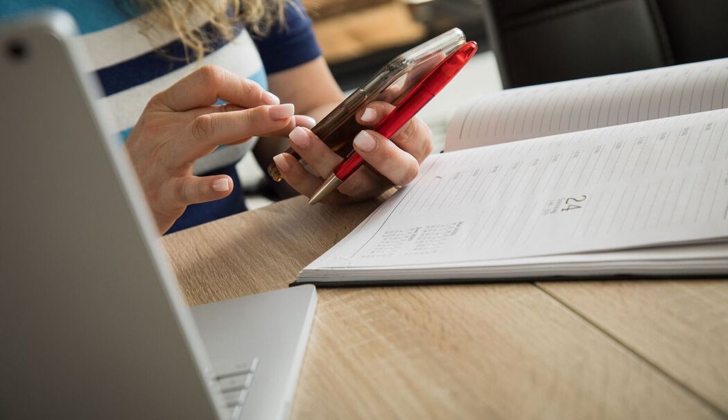 Frau schaut an ihrem Schreibtisch auf ein Smartphone