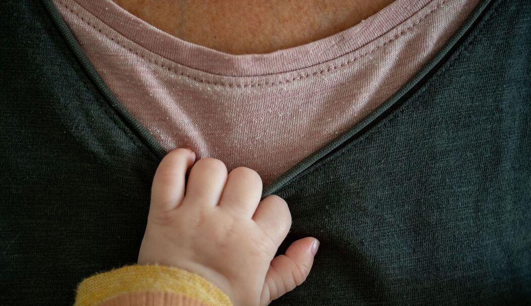 Ein Baby hält sich am T-Shirt der Mutter fest