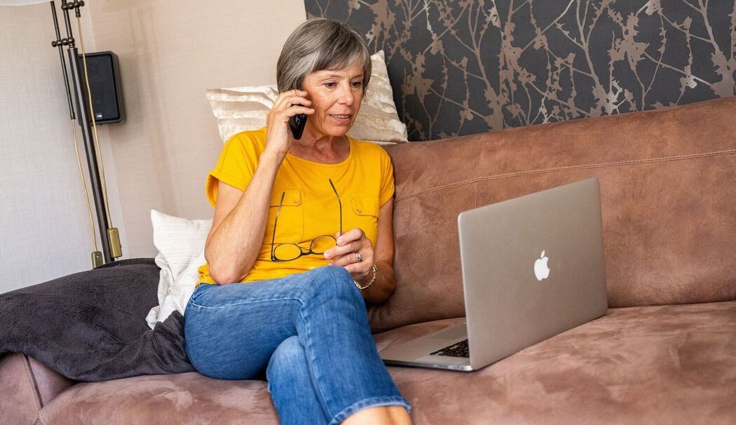 Eine ältere Frau telefoniert und schaut auf ihren Laptop