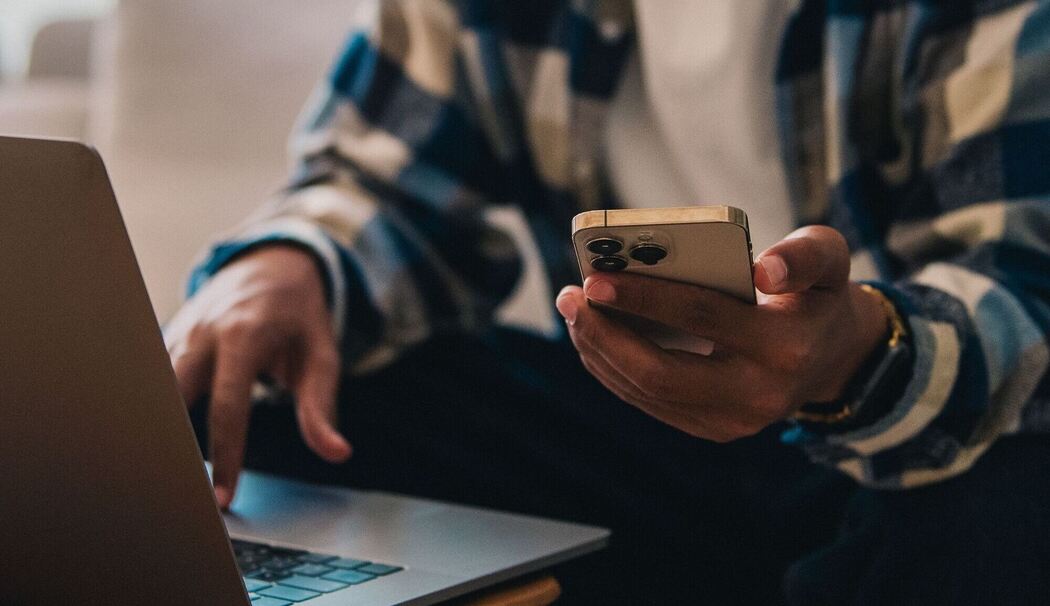 Ein Mann arbeitet am Laptop und hält ein Smartphone in der Hand