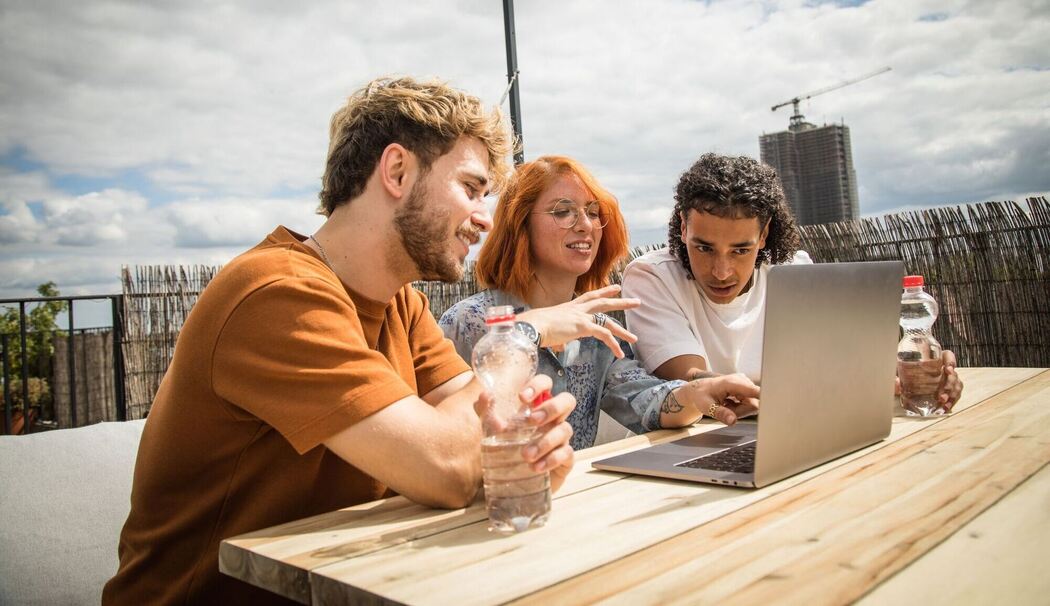 Junge Leute sitzen auf einer Dachterrasse vor einem Laptop