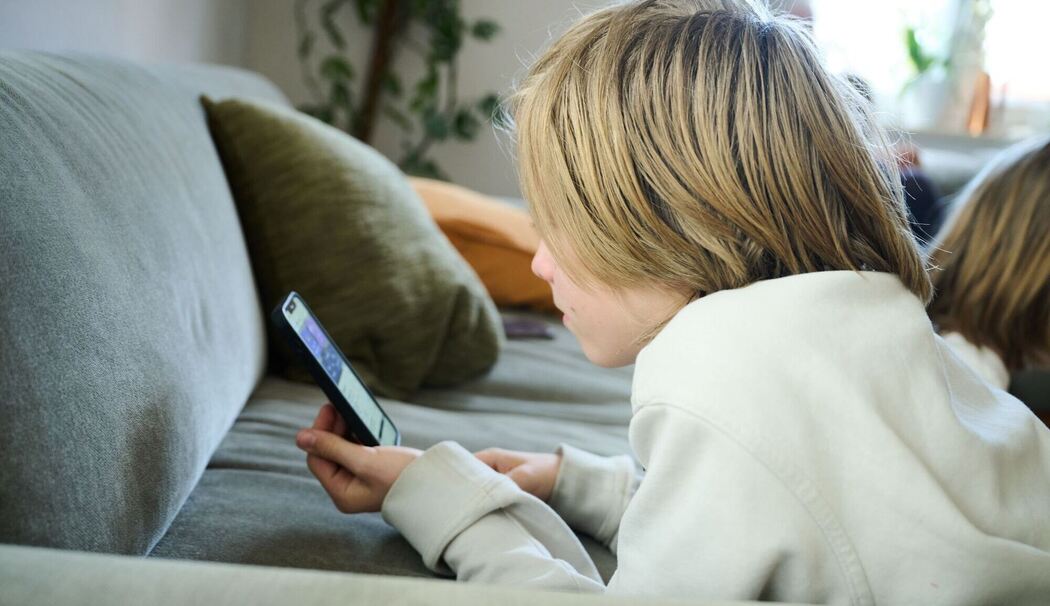 Ein Junge liegt auf einem Sofa und guckt auf sein Smartphone