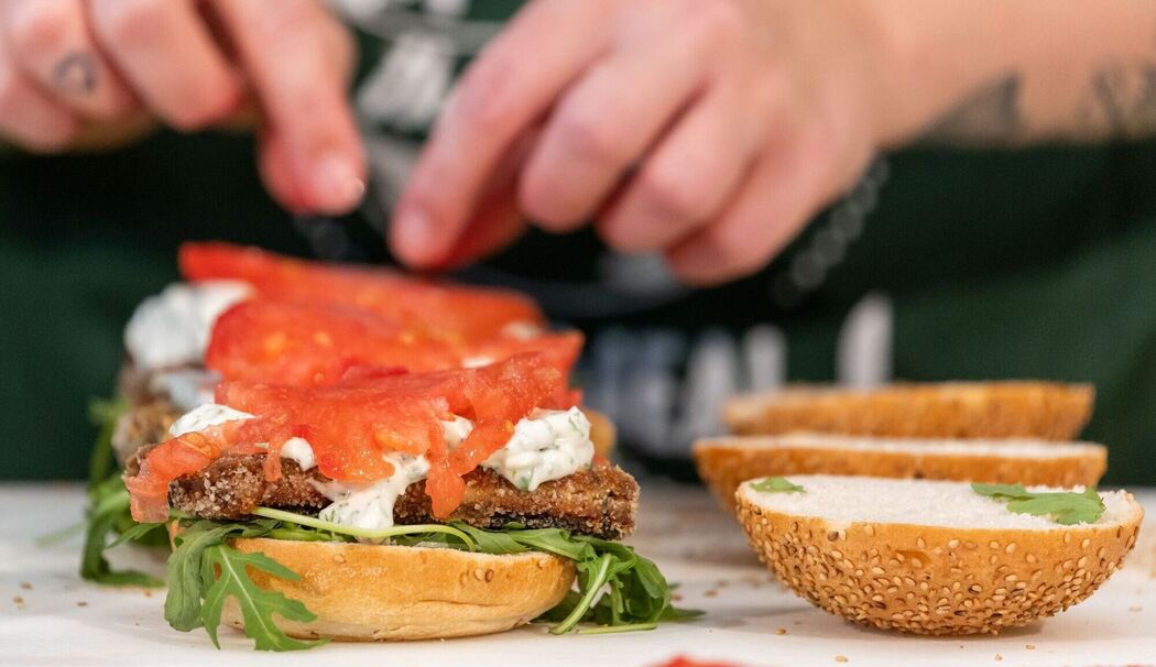 Eine Köchin belegt einen Burger mit veganem Fischersatz