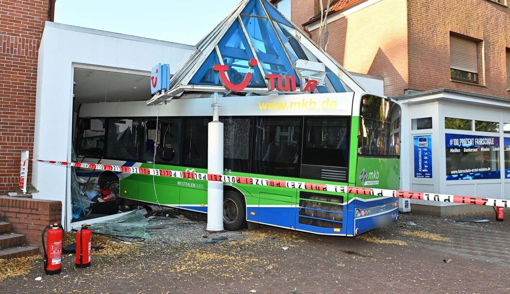Bus kollidiert mit Auto und kracht in Reisebüro