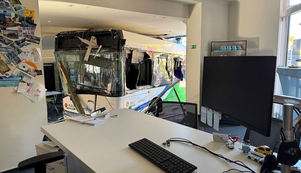 Bus kollidiert mit Auto und kracht in Reisebüro