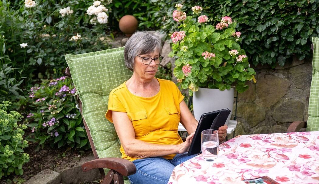 Eine Seniorin sitzt mit einem Tablet im Garten