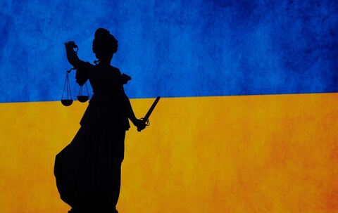 Eine Justitia-Figur vor der ukrainischen Flagge