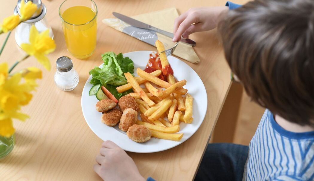 Ein Kind isst Chicken Nuggets und Pommes Frites