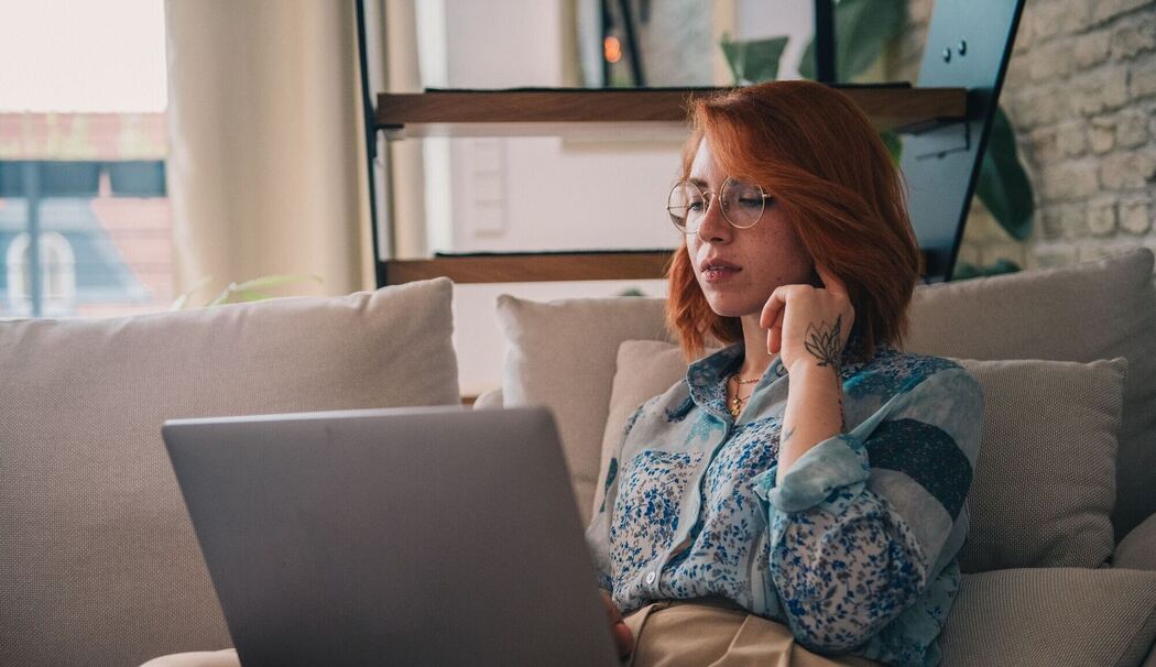 Eine Frau sitzt auf der Couch und nutzt einen Laptop