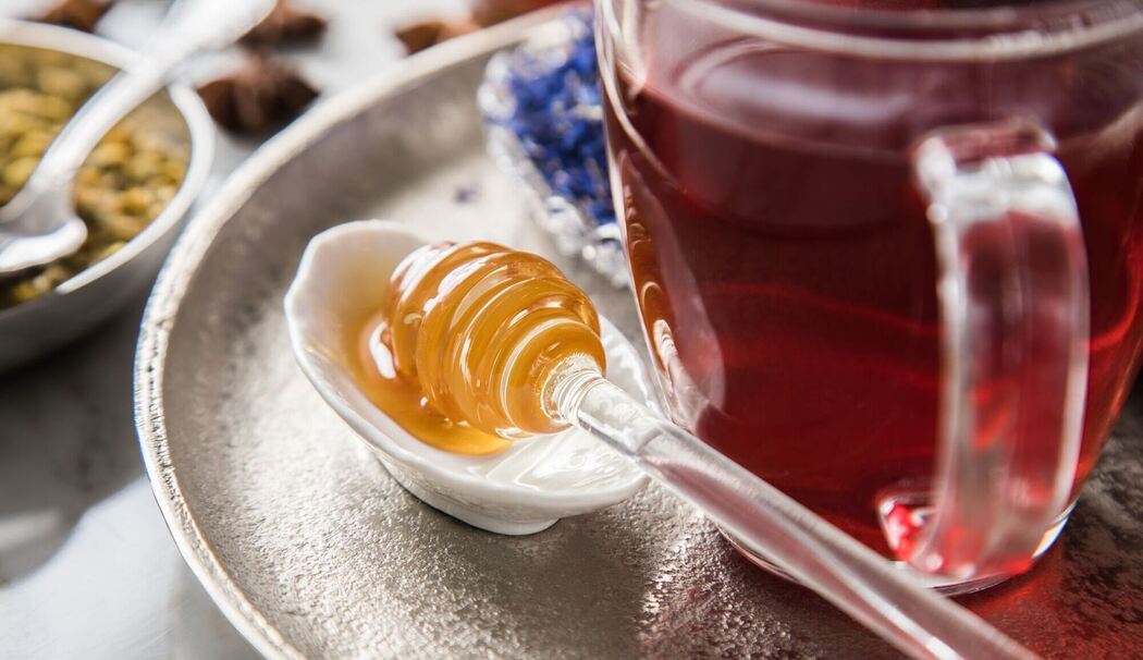 Ein Honiglöffel mit Waldhonig liegt neben einer Tasse Tee
