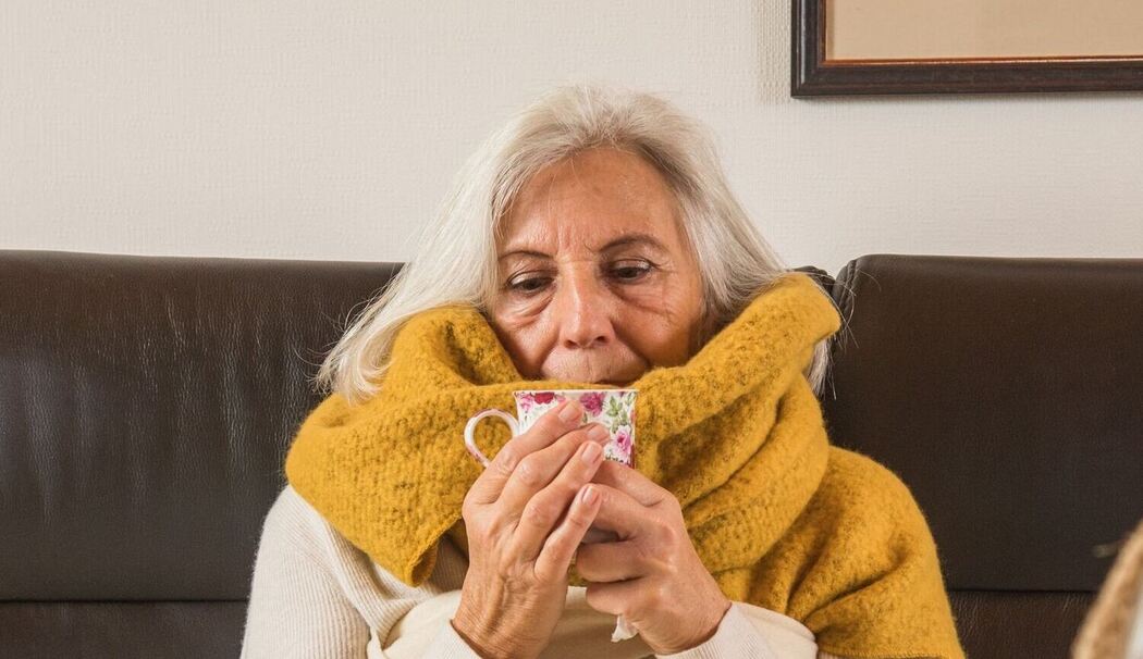Eine Frau mit Erkältung trinkt Tee auf einem Sofa
