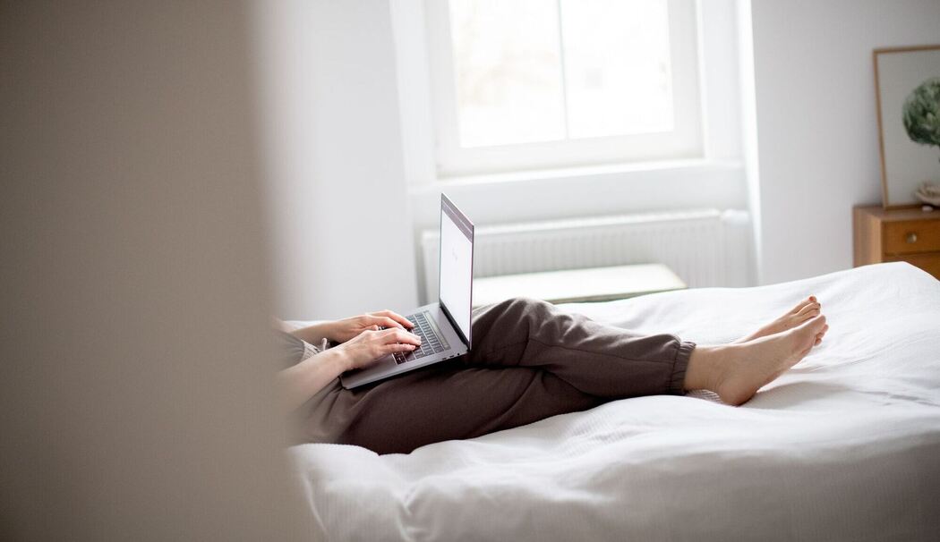 Eine Frau sitzt mit Laptop im Bett