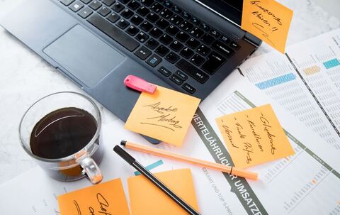 Chaos auf dem Schreibtisch mit Laptop, USB-Stick und Notizen