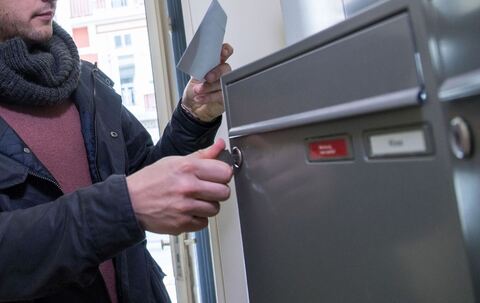 Ein Mann holt einen Brief aus dem Briefkasten
