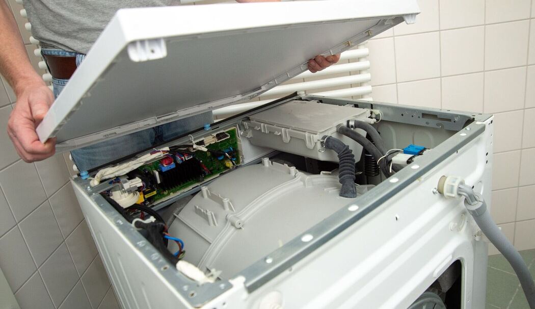 Ein Mann öffnet eine defekte Waschmaschine