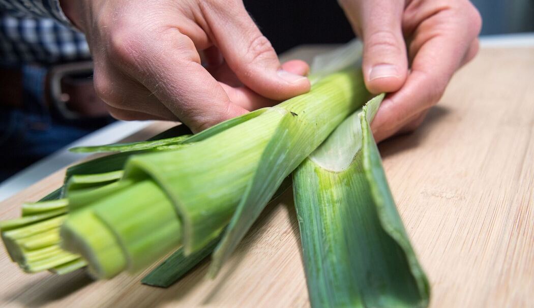 Mann entfernt die äußeren Blätter einer Lauchstange