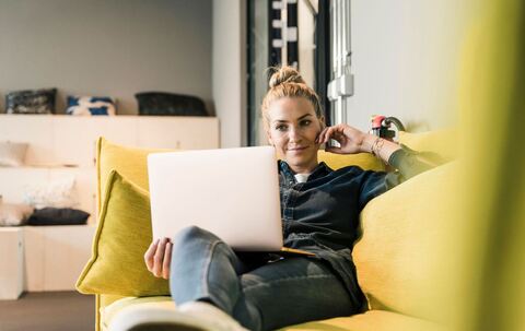 Frau sitzt mit Laptop auf einer Couch