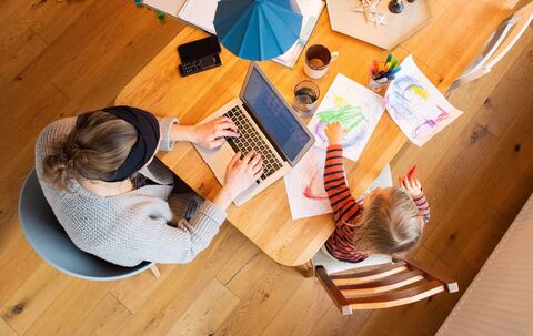 Eine Frau arbeitetneben ihrem Kind am Laptop