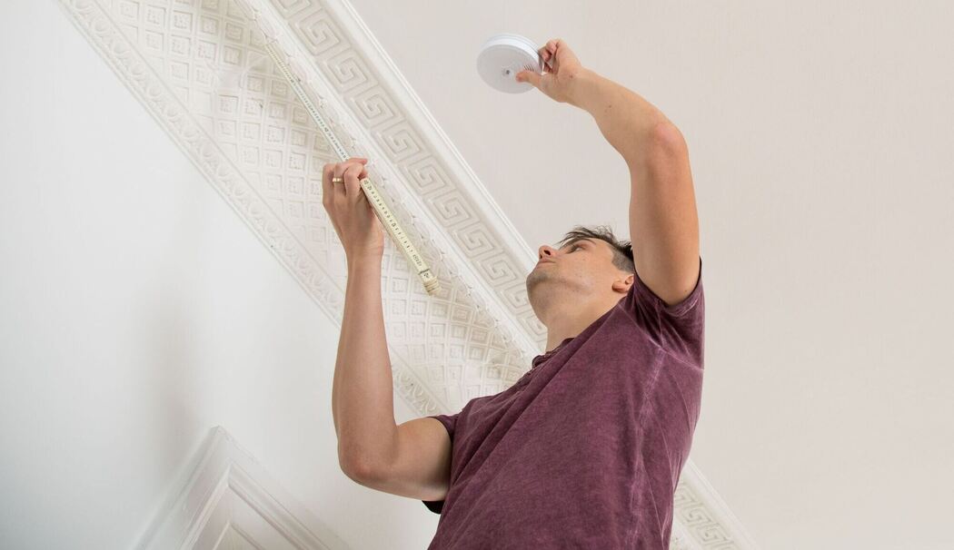 Ein Mann bringt einen Feuermelder an Ein Mann bringt einen Feuermelder an