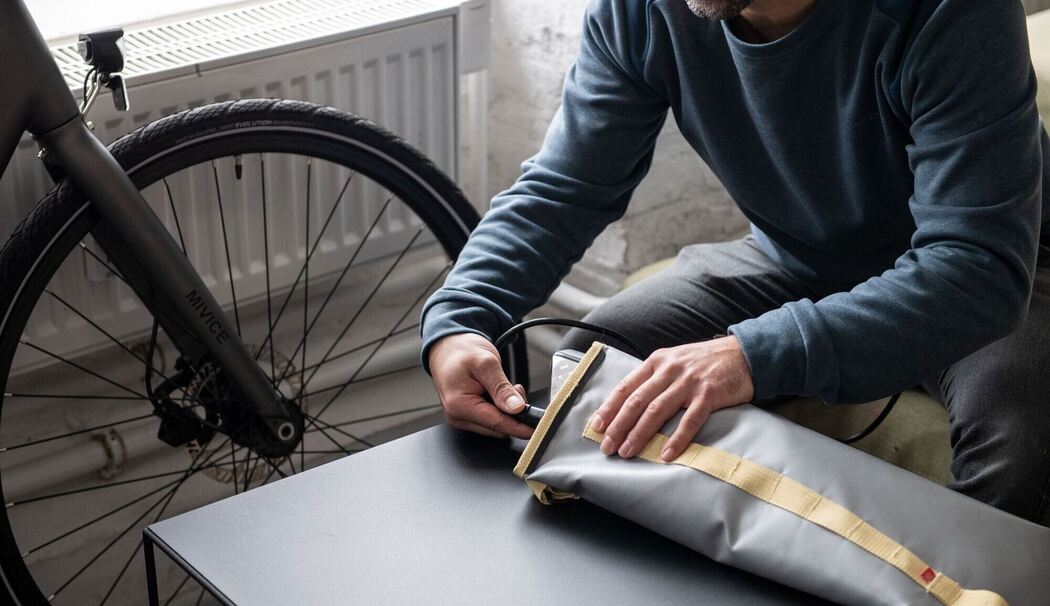 Ein Mann lädt einen E-Bike-Akku in einer feuerfesten Akku-Tasche Ein Mann lädt einen E-Bike-Akku in einer feuerfesten Akku-Tasche