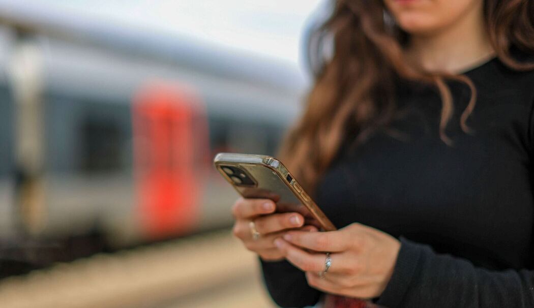 Eine junge Frau steht mit ihrem Mobiltelefon auf einem Bahnsteig
