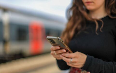 Eine junge Frau steht mit ihrem Mobiltelefon auf einem Bahnsteig