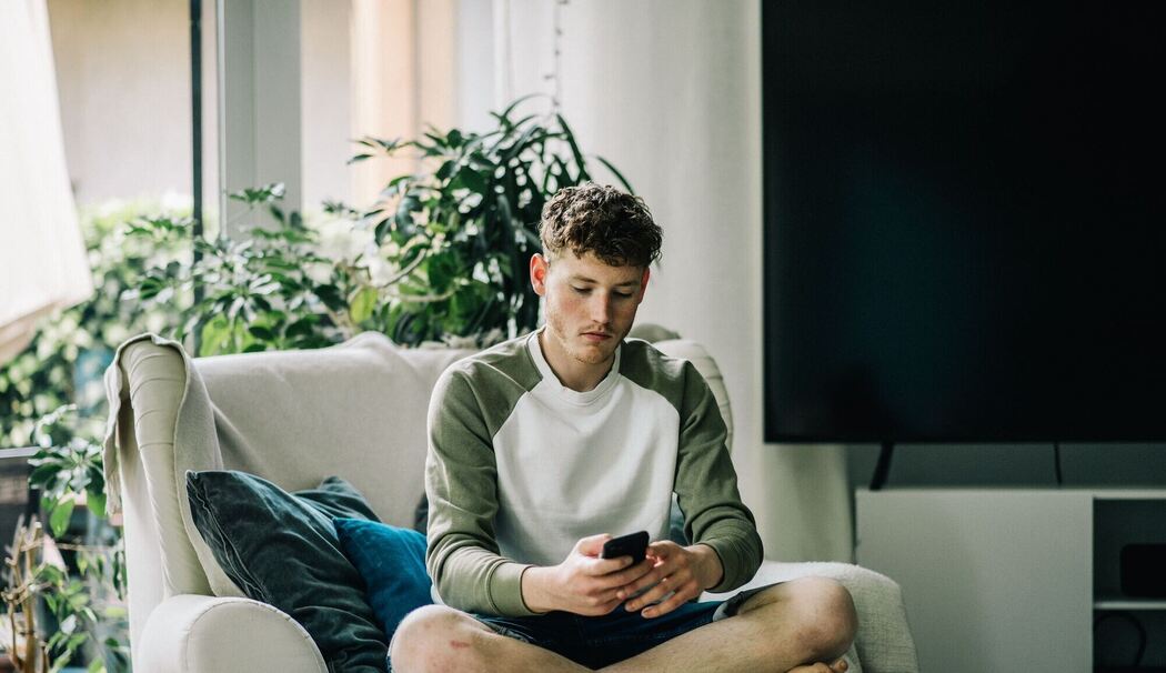 Ein junger Mann sitzt mit Smartphone auf einem Sessel Ein junger Mann sitzt mit Smartphone auf einem Sessel