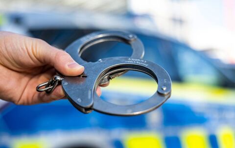 Handschellen vor Polizeiwagen - Symbolbild