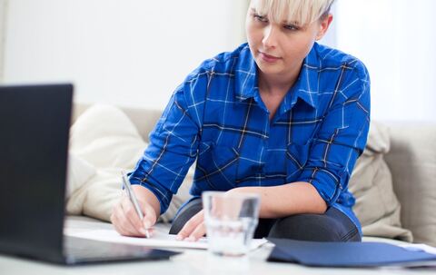 Frau macht sich neben einem Laptop Notizen