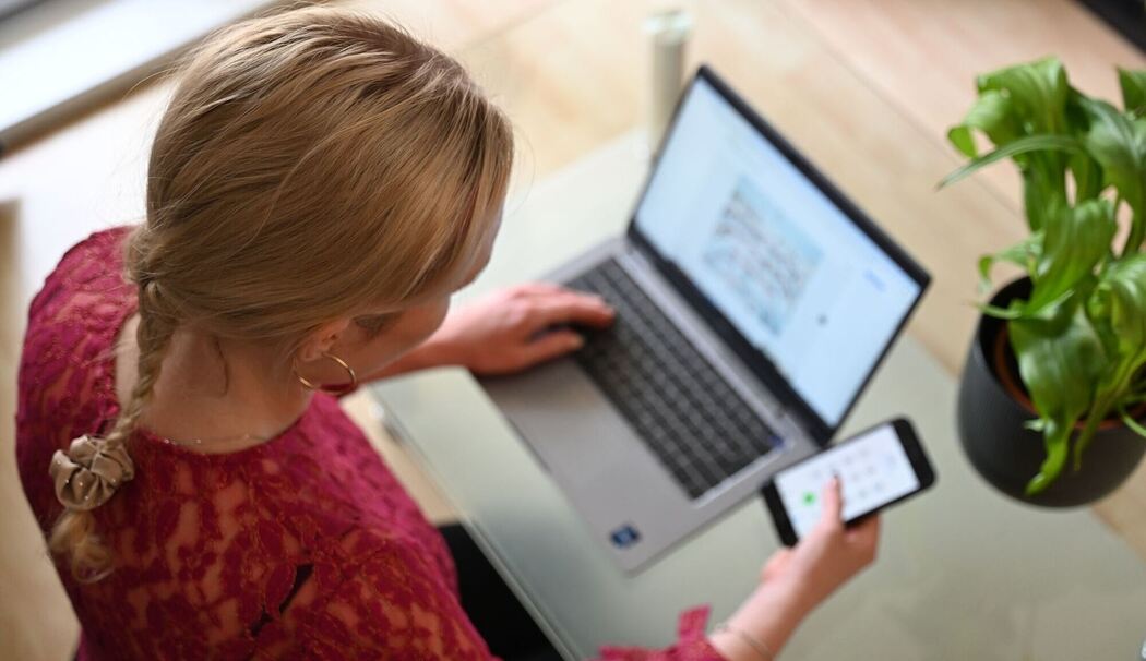 Frau sitzt vor Laptop und schaut auf Smartphone
