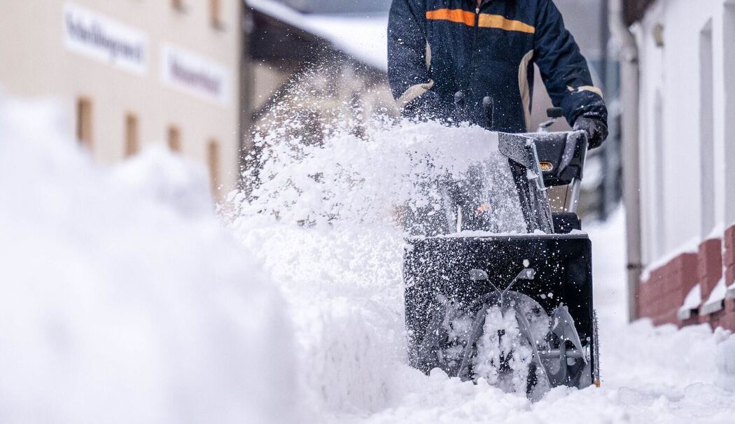 Ein Mann beräumt den Gehweg mit einer Schneefräse