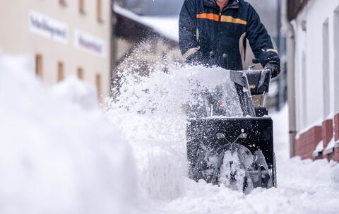 Ein Mann beräumt den Gehweg mit einer Schneefräse
