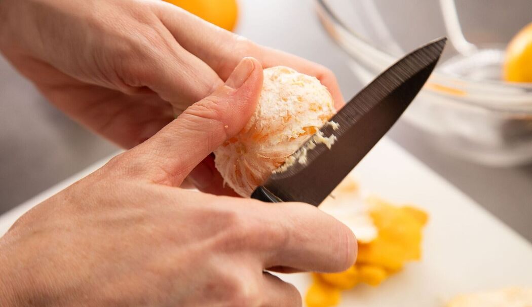 Eine Clementine wird mit einem Messer geschält