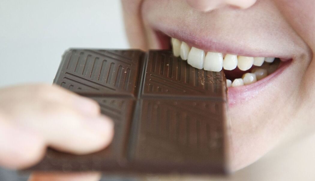 Frau beißt in ein Stück Schokolade Frau beißt in ein Stück Schokolade