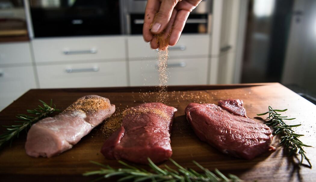 Eine Perosn würzt Fleisch Eine Perosn würzt Fleisch