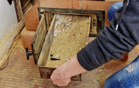 Eine Frau entnimmt die Ascheschublade aus einem Kachelofen