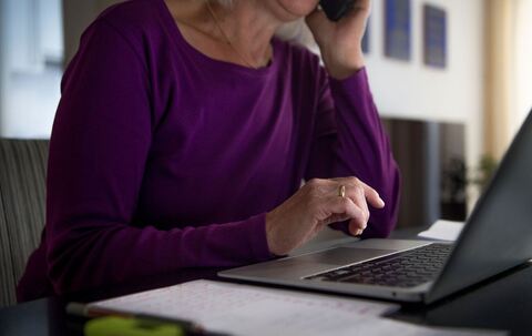 Eine Frau sitzt zu Hause an einem Esstisch am Laptop