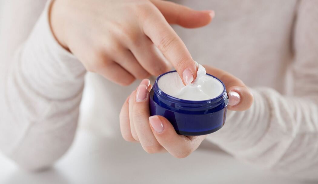Eine Frau streicht mit dem Finger durch eine Cremedose