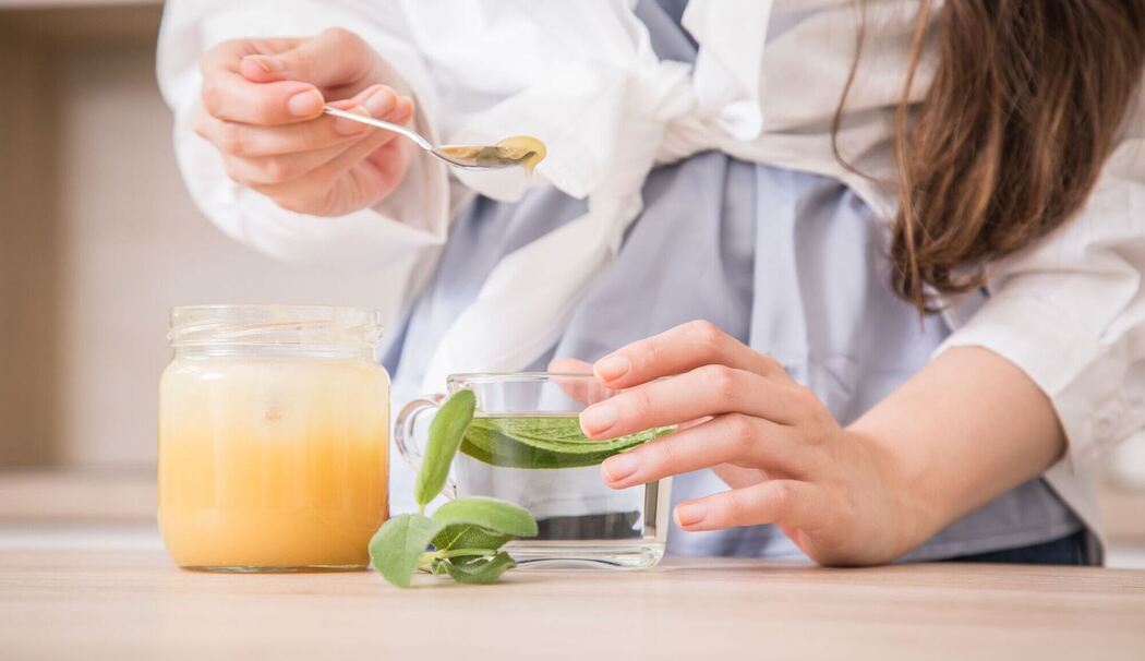 Eine Frau bereitet frischen Salbeitee mit Honig zu