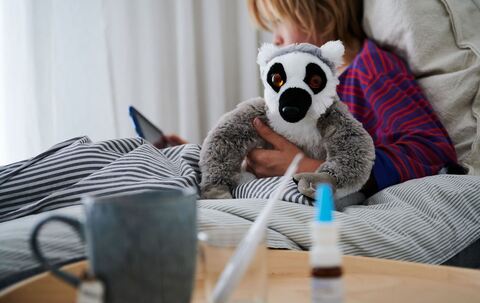 Krankes Kind liegt mit einem Kuscheltier im Bett
